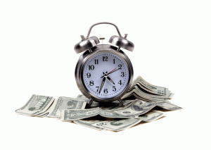 A silver analog alarm clock resting on a small pile of money