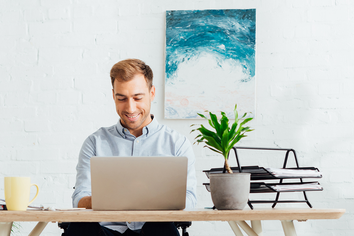 Smiling freelancer/remote worker using laptop computer while sitting at desk in living room.