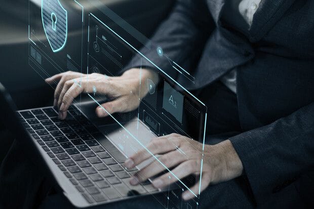 Business professional typing on a laptop with a glowing holographic security shield and AI dashboard interface