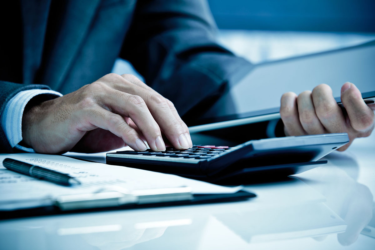 Businessman seated at desk with close up of hands using calculator, business analysis/accounting concept.