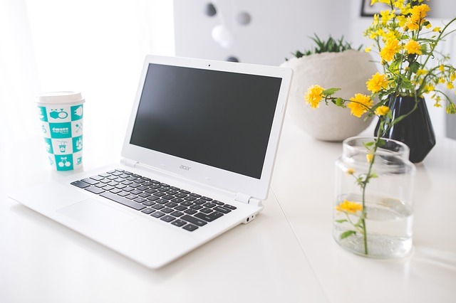 White Acer laptop sitting on a white table, with a yellow flower in a glass to the side