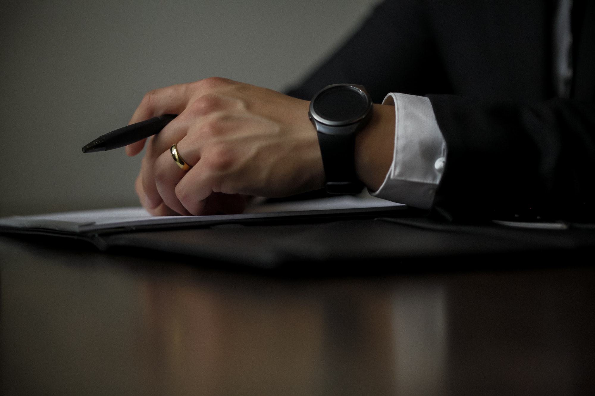 Close of up businessman's holding a pen, wearing a black watch and a gold wedding band