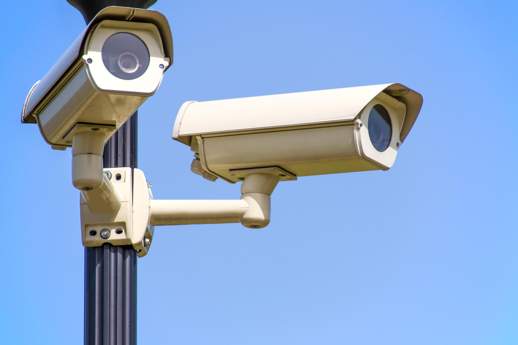 Two CCTV security cameras on a pole with a blue sky behind them