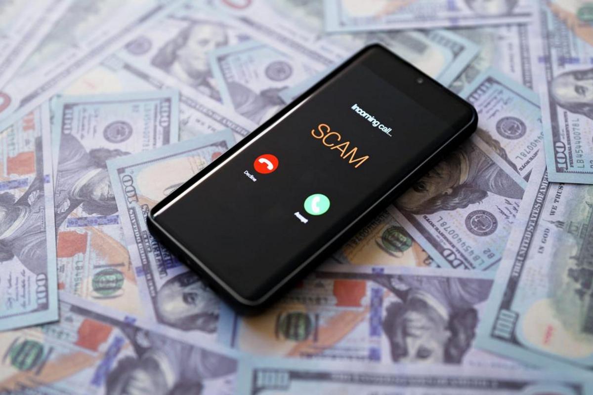 Smartphone showing an incoming call labeled SCAM on a pile of hundred-dollar bills