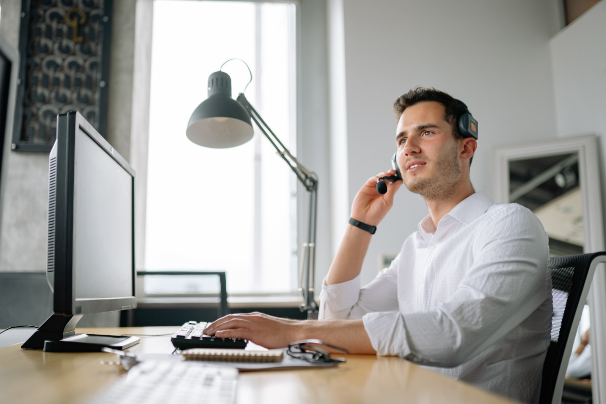 A man in a white shirt wearing a headset while working at at his computer