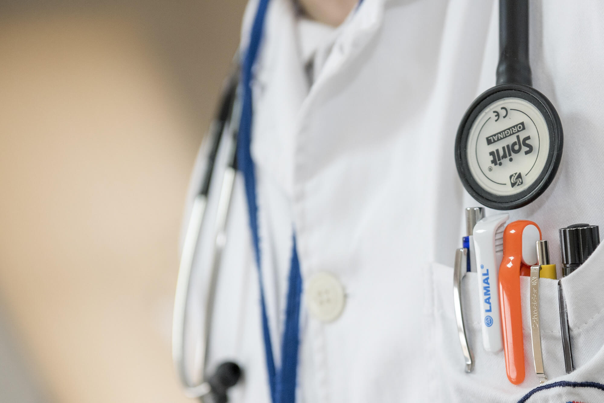 Doctor in white scrubs wearing a stethoscope and with a pocket full of pens