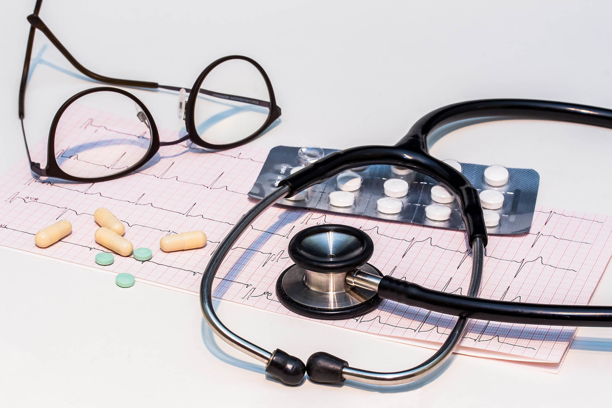 Stethoscope, glasses, and pills resting on a paper ECG readout