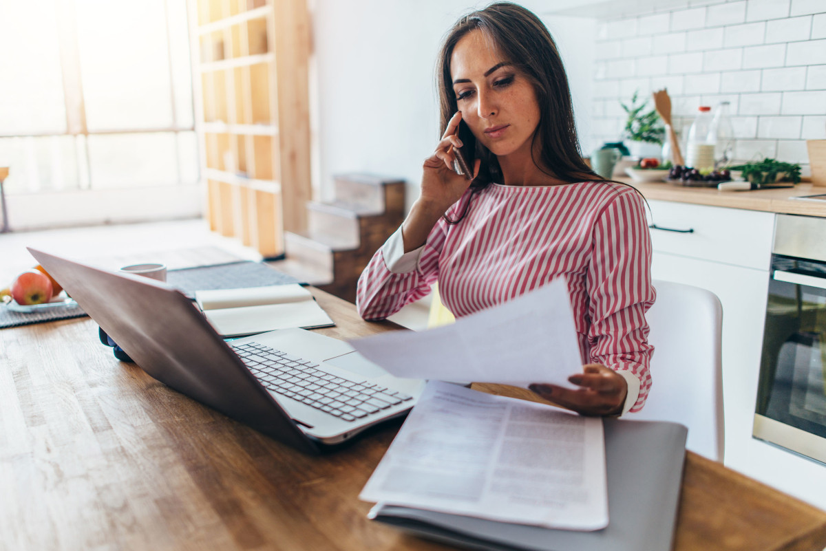 Woman on Phone, Using Laptop, and Looking Over Papers in Home Office