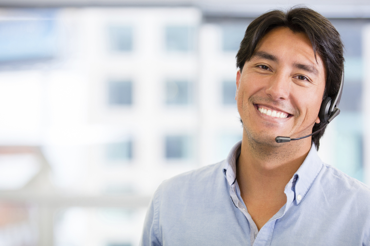A smiling person with a desk phone headset on