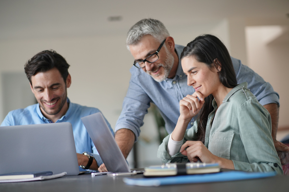 Young colleagues with older boss working with computers in shared workspace.