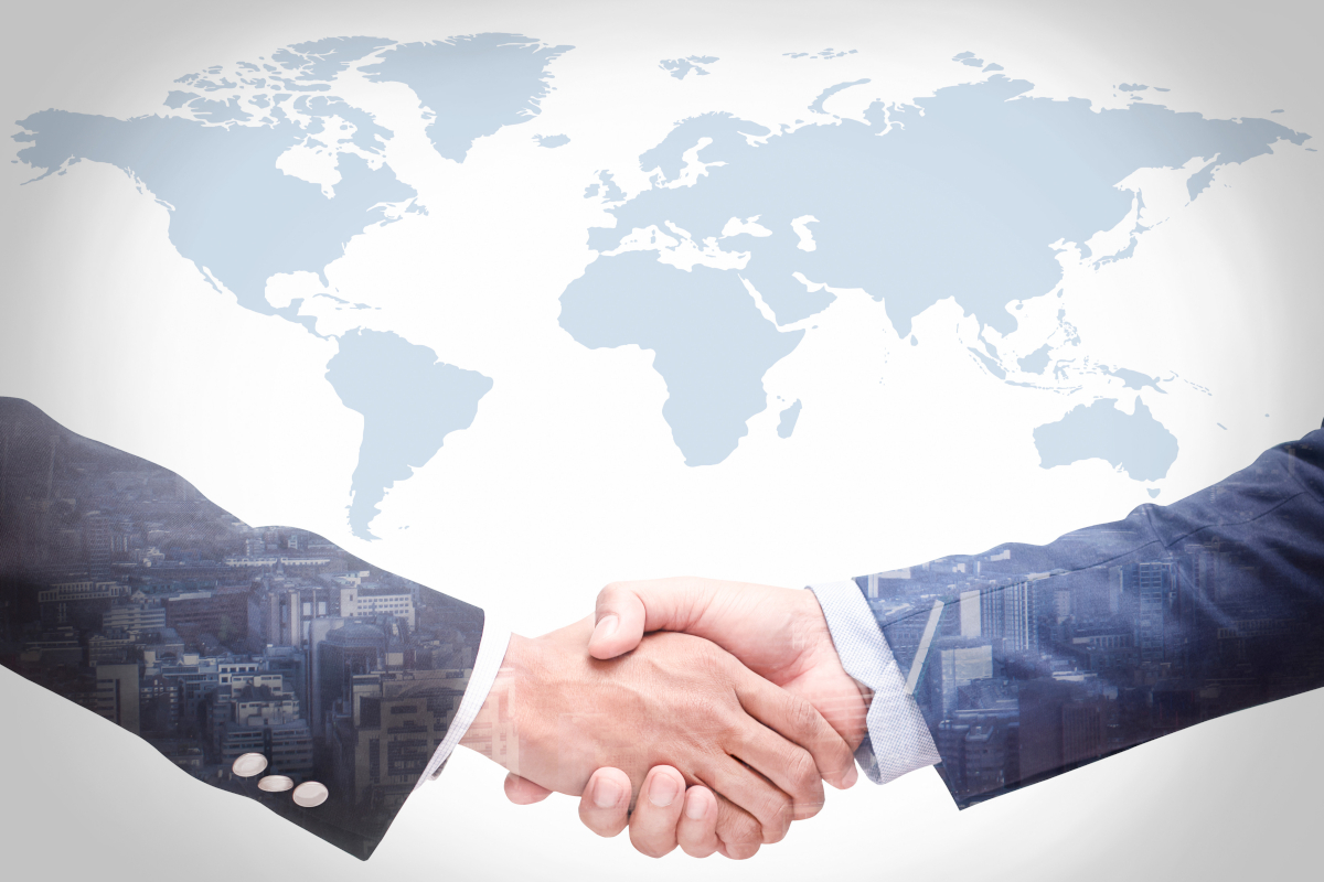 A handshake between businessmen with a world map in the background and a city skyline visible on their sleeves.