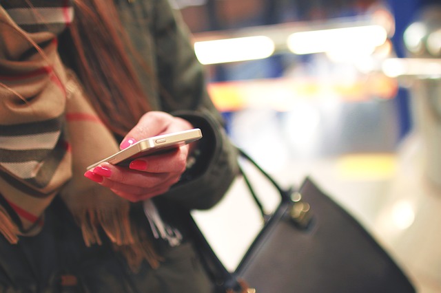 Close up of a woman with pink fingernails using an iPhone while carrying a black bag