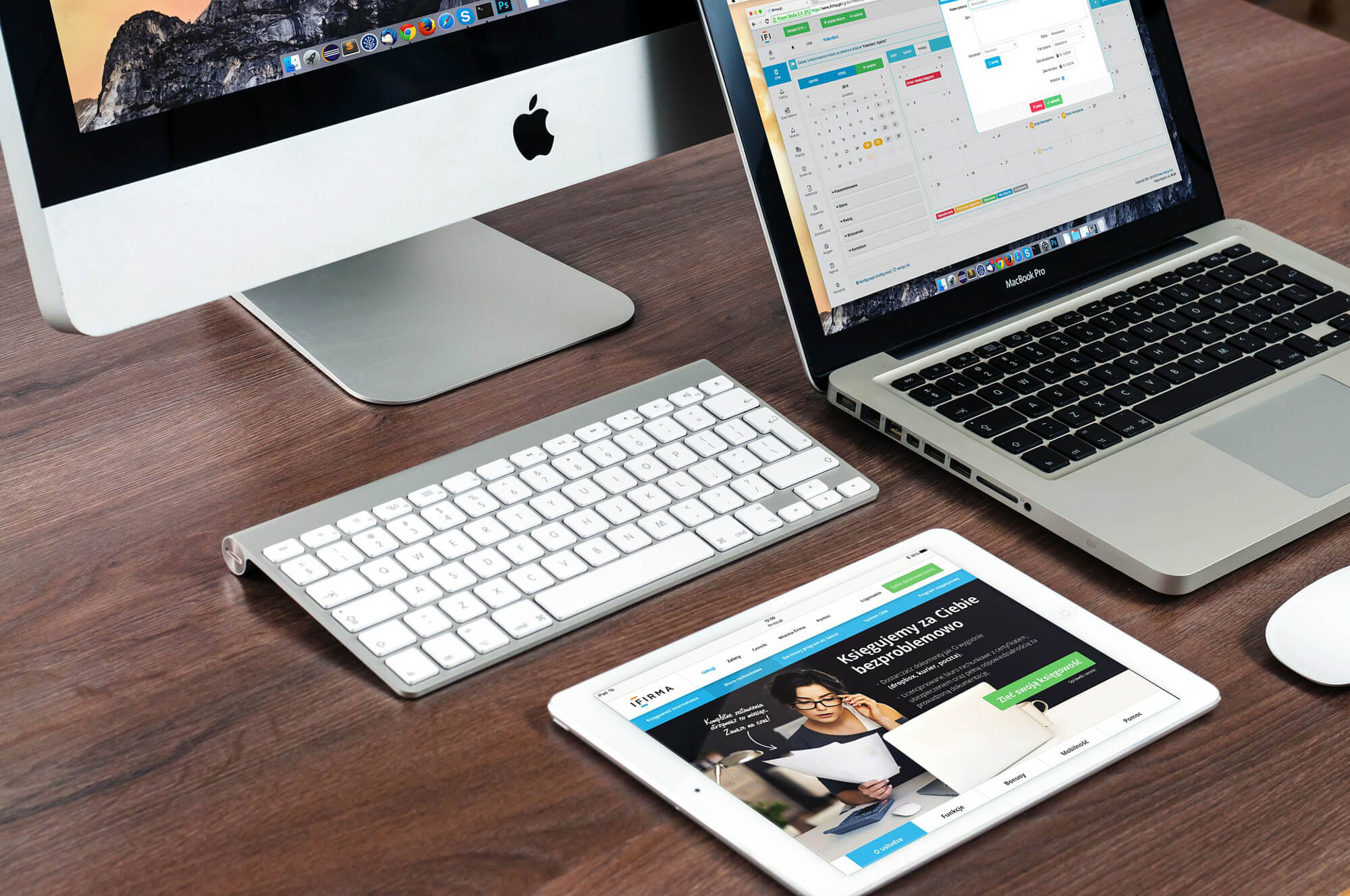 Dark wood desk with a Mac desktop, a gray MacBook Pro, and a white table resting on it