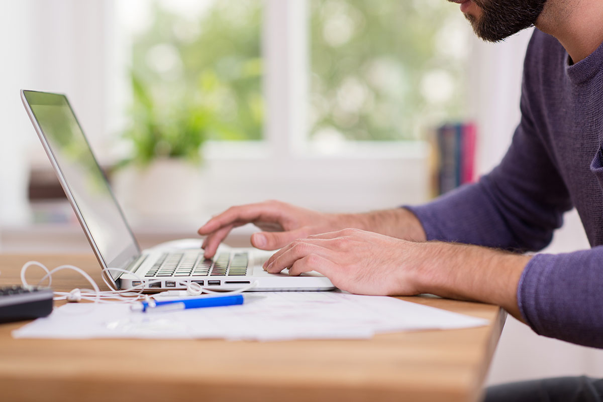 Close up of worker's hands using laptop computer at desk in home office.