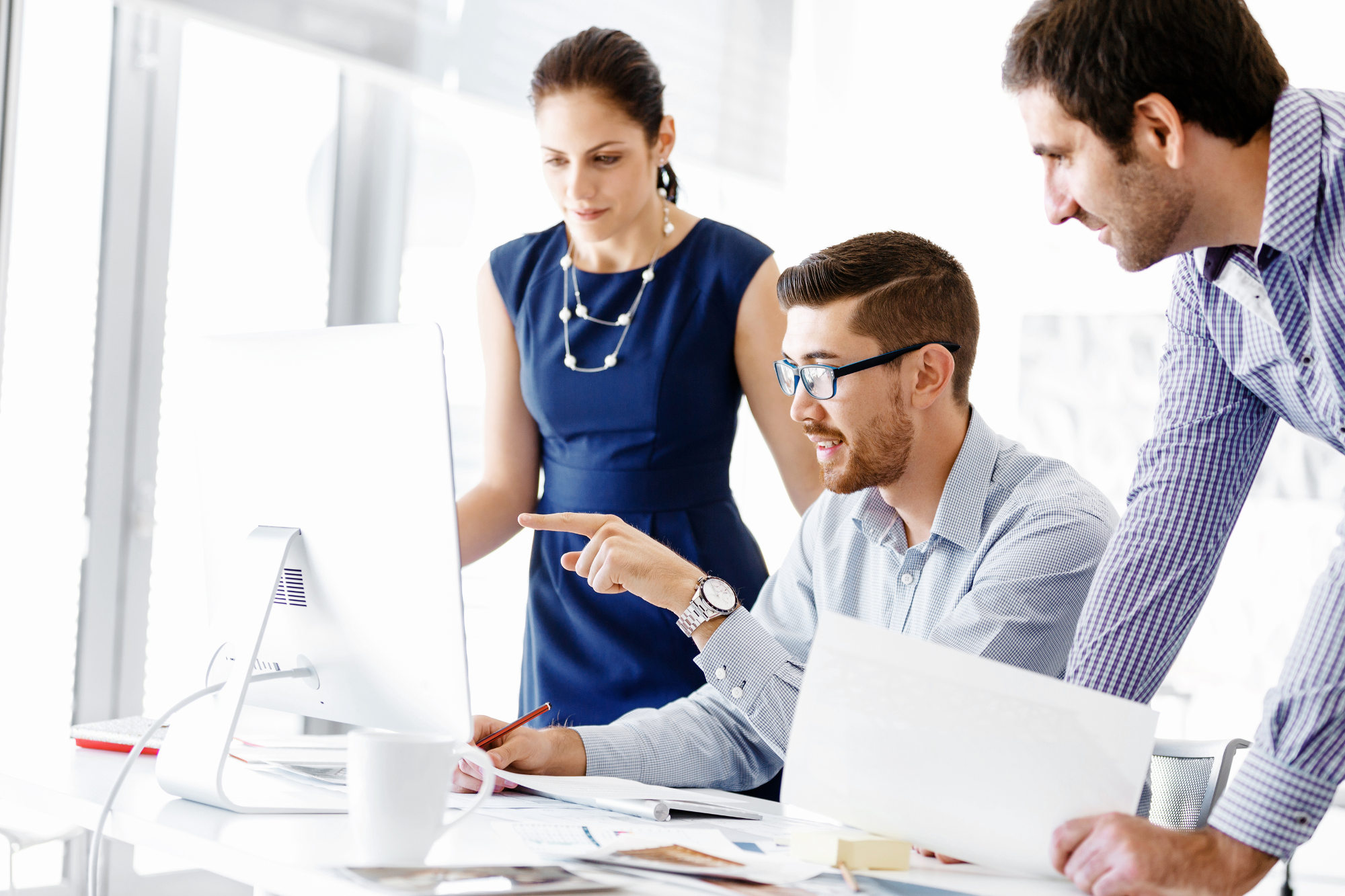 Business woman and two male colleagues gathered around a monitor