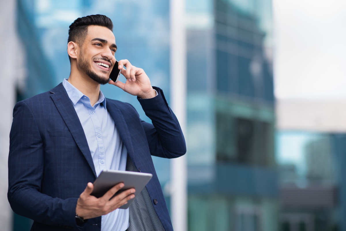 Smiling man talking on a mobile phone while holding a laptop