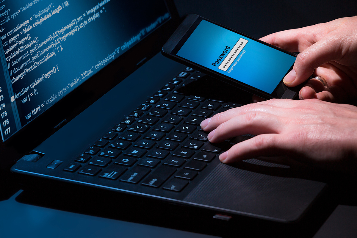 Close up of hands using laptop and mobile phone, two-factor authentication, cyber security, password protection concept.
