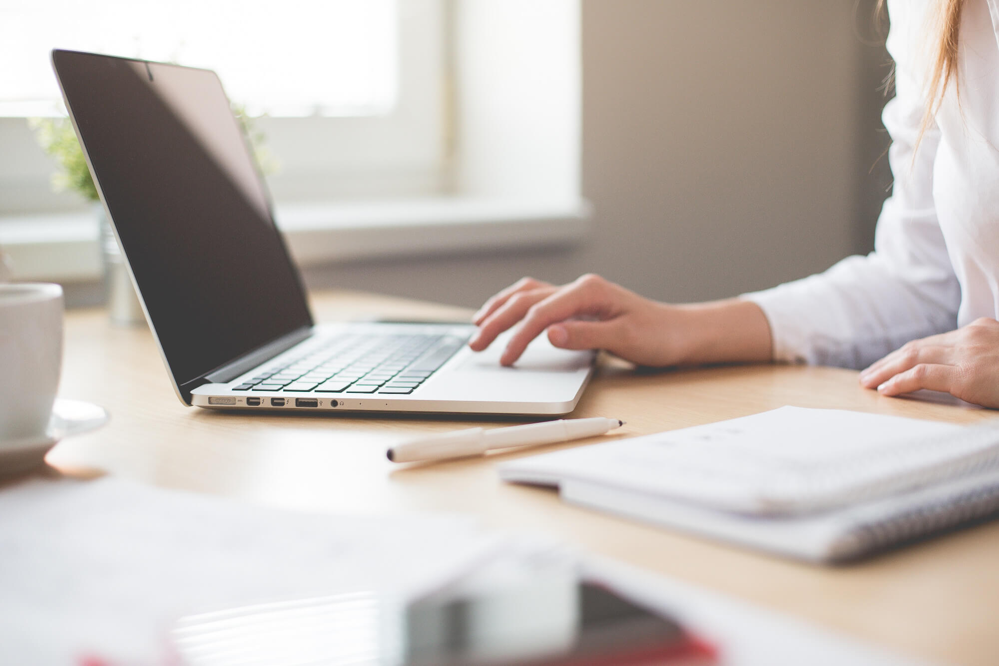 White-bloused businesswoman using a slim laptop on a birch colored desk