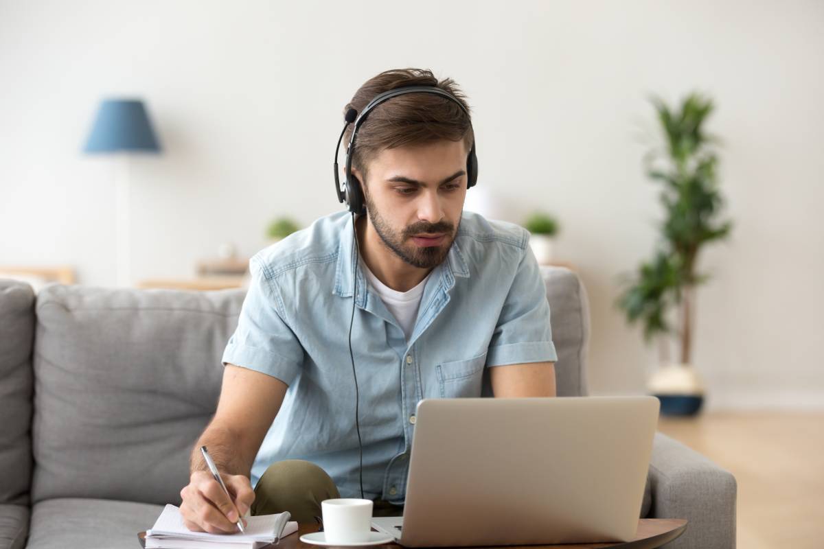 A man working from home on his laptop while sitting on a sofa with a headset on