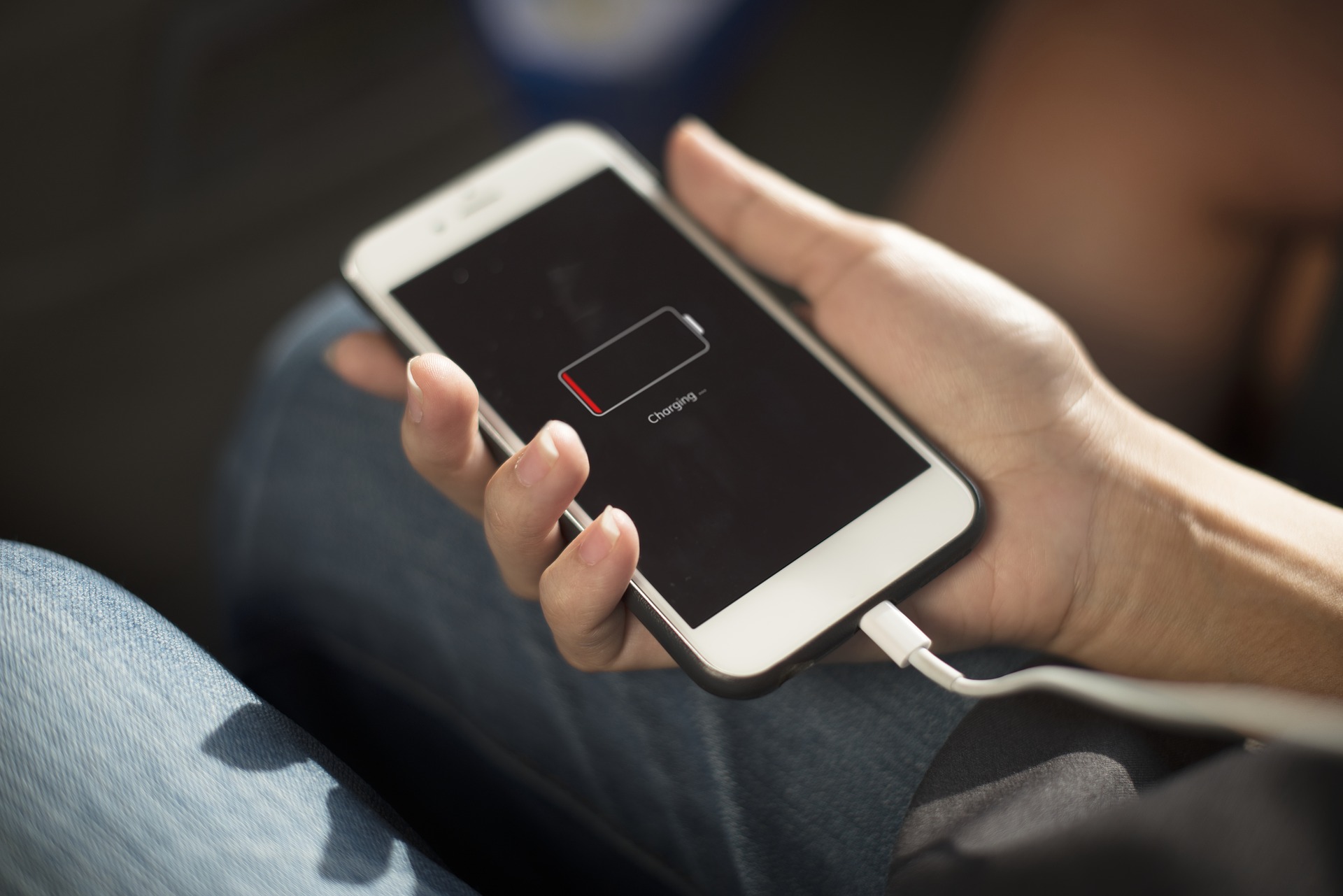 Hand holding a white iPhone plugged in and charging from empty