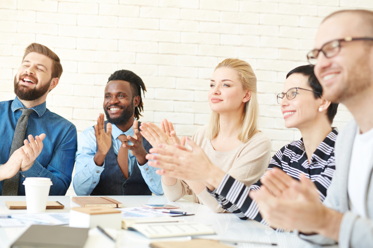 Business team seated around conference table in applause.