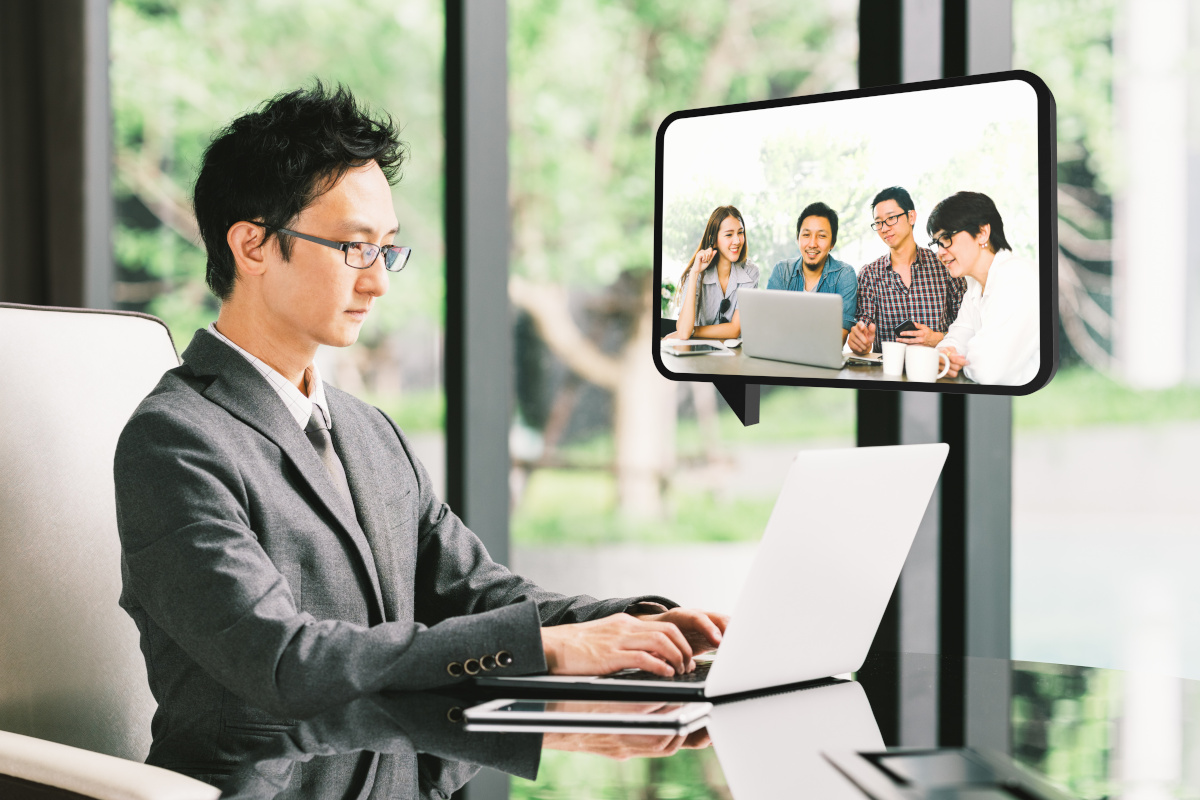 A person on laptop with another monitor displaying a video call