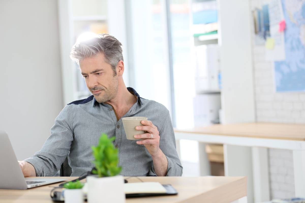 A man working from home using a laptop and drinking coffee