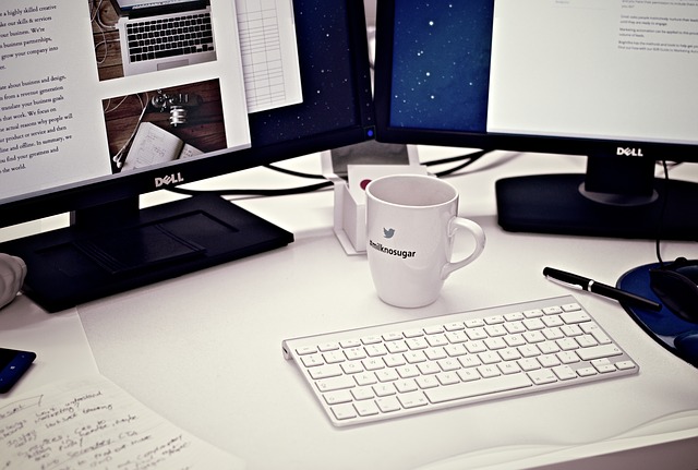 White office desktop with 2 Dell monitors and an Apple keyboard around a coffee cup