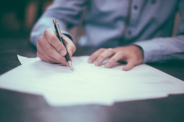 Businessman reviewing 3 papers while poised to write on one with a fancy pen