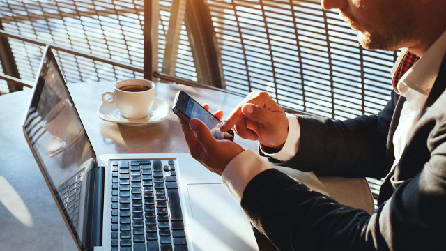 Business Man Using Cell Phone with Laptop and Coffee on Table