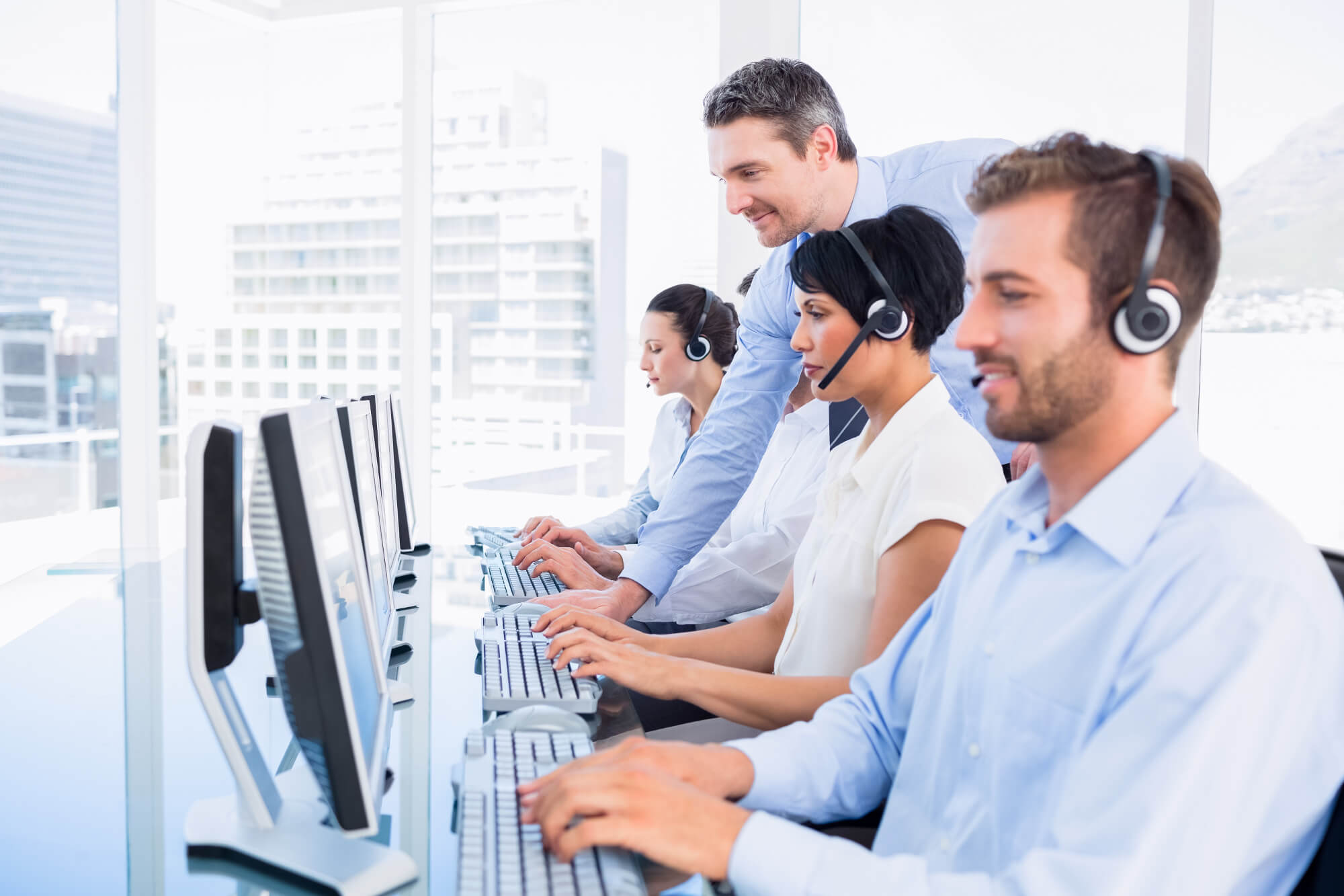 Customer Service Reps on Computers while Man with Salt and Pepper Hair Overlooks Them