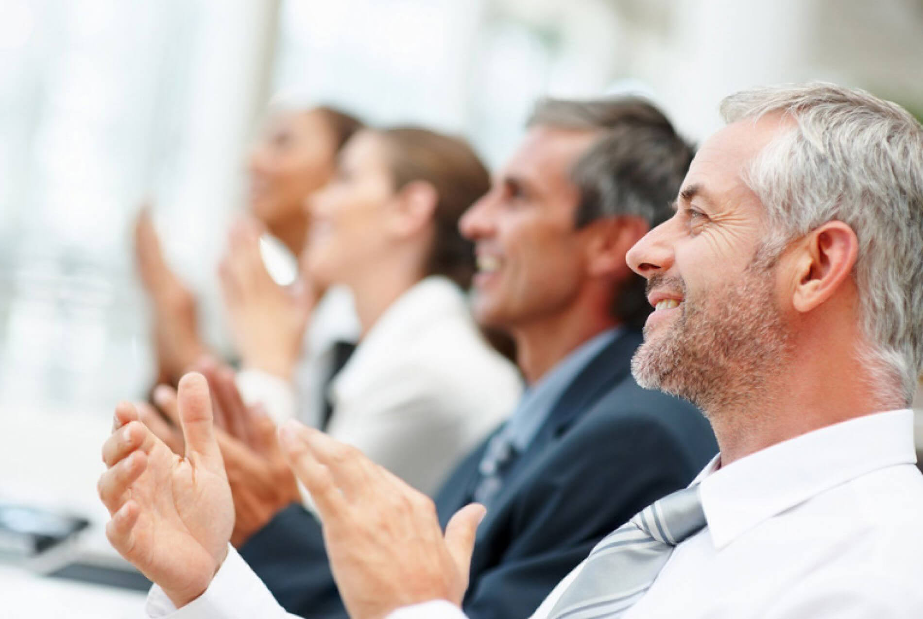 Close Up of Mature Businessman with Additional People Blurred in Background Clapping