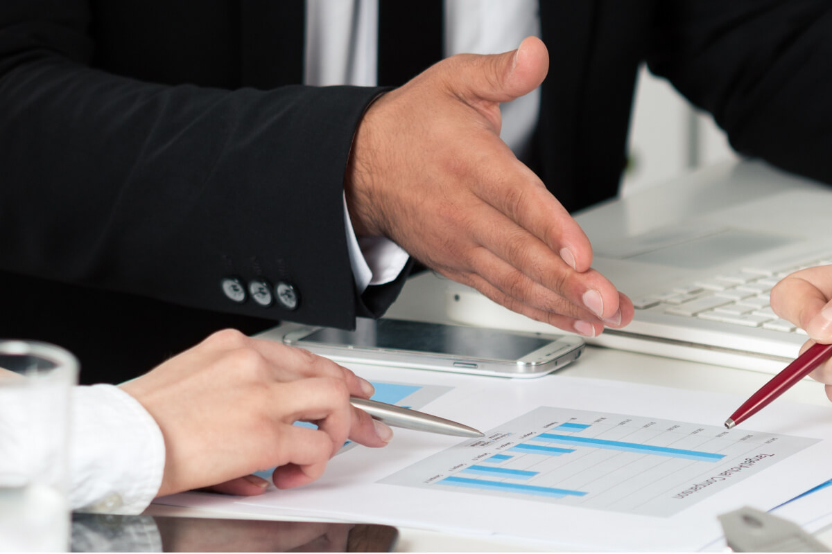 Close Up of Hands Around Meeting Table Gesturing at Chart