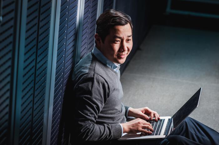 Man Leaning Against Server Cabinets with Laptop Computer in Lap