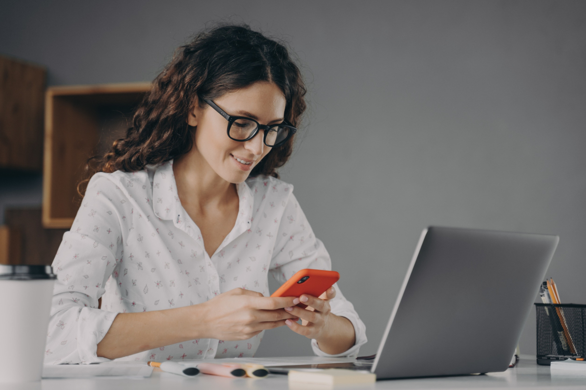 Woman working from home on a laptop while also using her smartphone