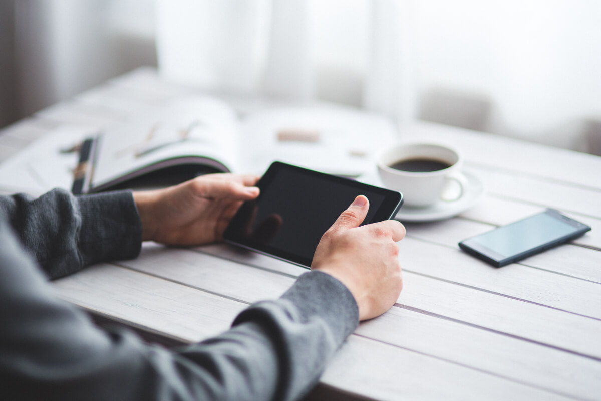 Close Up of Hands Holding Tablet with Cell Phone and Cup of Coffee on Table